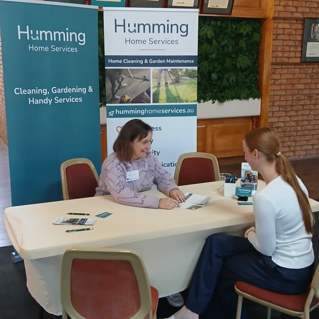 Humming Home Services team member talking with a visitor at a community event table with Humming banners