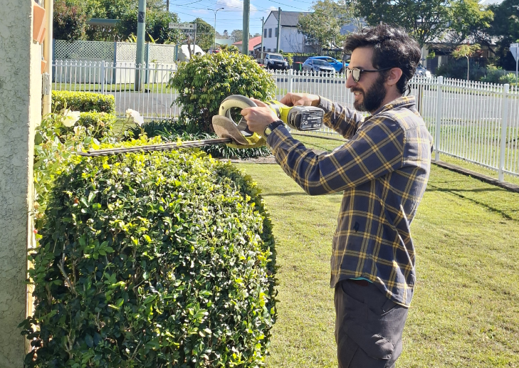 NDIS gardener trimming a round hedge with electric hedge trimmers in a Queensland front yard