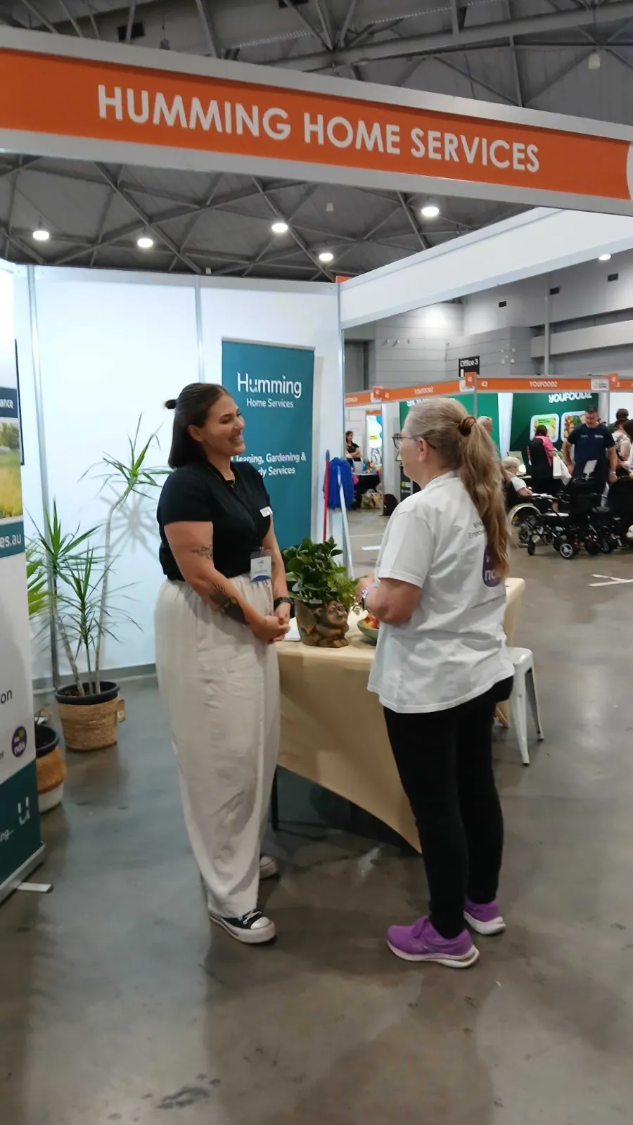 Humming Home Services team member chatting with a visitor at the company booth at the Brisbane Disability Expo in South Brisbane